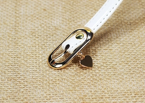 Close-up of white patent leather belt with golden oval buckle and heart charm detail