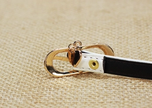 Close-up of golden oval buckle with heart pendant and rivet on contrast leather belt