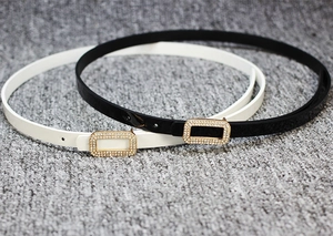 Close-up of black and white skinny patent leather belts with rhinestone buckle