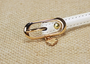 Close-up of a white patent leather belt with a gold oval buckle and heart-shaped charm