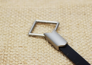 Macro shot of a minimalist silver square metal buckle with a smooth black leather strap