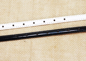 Detail of glossy patent leather belts in black and white with stitching and pin buckle
