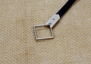 Detail of minimalist black leather belt showing silver square buckle and hardware