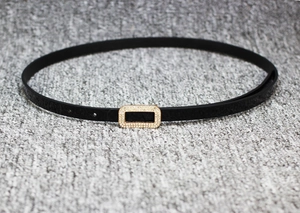 Macro detail of glossy black patent leather belt with a rectangular gold rhinestone buckle