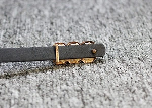 Close-up of black skinny leather belt with gold rectangular buckle and metal hardware