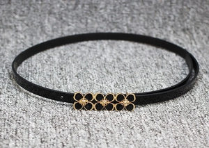 Détail d'une fine ceinture en cuir verni noir avec boucle triple fleur dorée élégante