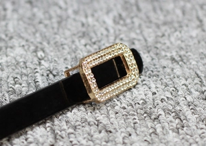 Detail shot of a slim black patent leather belt with a rectangular gold rhinestone buckle