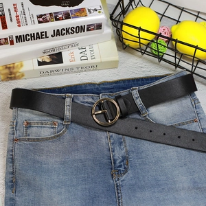 Vue détaillée d'une ceinture en cuir noir avec boucle dorée ronde sur un jean bleu