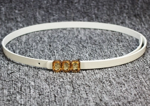 Detailed macro view of white patent leather belt with amber gemstones on gold buckle
