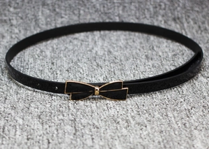 Détail d'une fine ceinture noire en cuir verni avec une boucle noeud dorée élégante