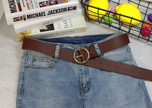 Détail de la ceinture en cuir marron avec boucle ronde dorée et couture sur un jean