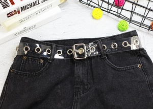 Close-up of a clear PVC belt with silver metal grommets styled on black denim jeans