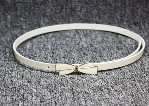 Détail de la fine ceinture en cuir verni blanc avec boucle nœud dorée et perforations