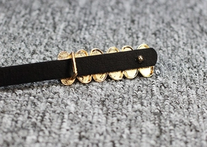 Détail d'une fine ceinture en cuir noir avec une boucle ovale en métal doré de style vintage
