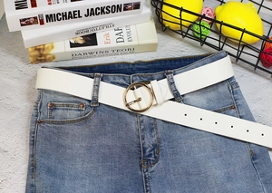 Détail d'une ceinture blanche en similicuir avec boucle ronde dorée sur un jean bleu