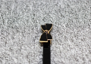 Détail d'une boucle de ceinture en cuir verni noir avec élégant bord doré et nœud papillon