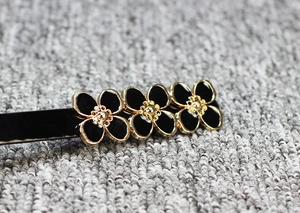 Vue détaillée de trois fleurs noires aux bords dorés métalliques sur une barrette à cheveux