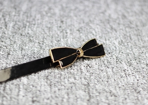 Détail d'une ceinture fine en cuir verni noir avec une boucle dorée en forme de nœud