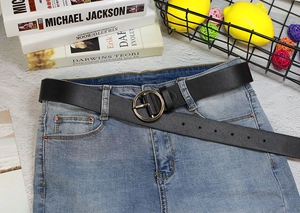 Détail d'une ceinture en cuir noir avec boucle ronde dorée sur un jean en denim bleu clair