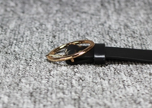 Gros plan d'une ceinture fine en cuir verni noir avec une boucle dorée ronde élégante