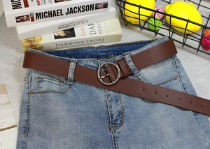 Détail de la ceinture en cuir marron foncé avec boucle ronde argentée sur jean bleu clair