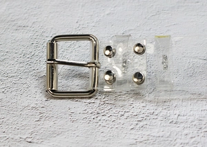 Detail of transparent PVC belt with square silver metal buckle and reinforced rivets