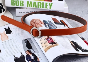 Flat lay of brown faux leather belt with silver round buckle on top of fashion magazines