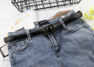 Close-up of black retro leather belt with square metal buckle on blue washed denim jeans