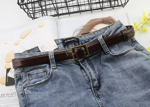 Close-up of dark brown slim leather belt with a vintage bronze square buckle on jeans
