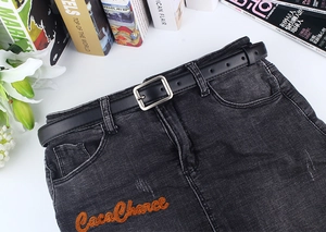 Detailansicht schwarzer schmaler Kunstledergürtel mit Silberschnalle auf Jeansrock