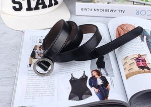 Close-up of a black faux leather belt with a round silver buckle on a stylish magazine