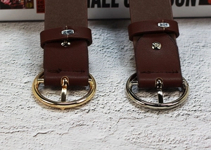Détail de la boucle ronde en métal sur ceinture en cuir marron foncé dorée et argentée