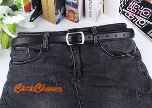 Detailansicht eines schwarzen Ledergürtels mit silberner Schnalle auf Denim-Kleidung