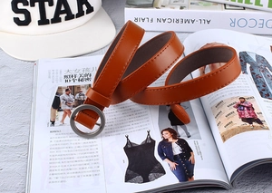 Detailed view of camel faux leather thin belt with round silver buckle on a magazine background