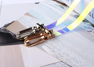 Dettaglio di cintura in PVC olografico trasparente con fibbie in metallo oro e argento