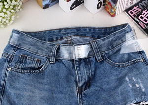 Detail of clear PVC belt with silver metal buckles on dark blue denim shorts
