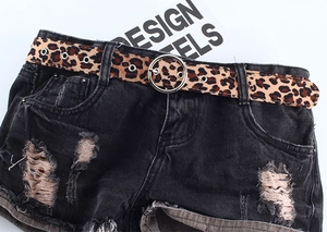 Détail d'une ceinture fine léopard avec boucle ronde en métal sur un jean noir