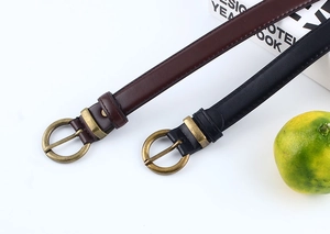Dettaglio di sottili cinture in pelle vintage con fibbie rotonde in bronzo nero e marrone