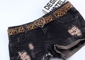 Détail de ceinture léopard avec boucle cœur argentée sur un short en jean noir usé