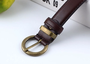 Dettaglio di una cintura in pelle marrone scuro con fibbia ad ardiglione tonda in metallo dorato