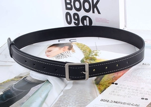 Détails d'une ceinture en cuir noir avec boucle argentée et surpiqûres blanches contrastées