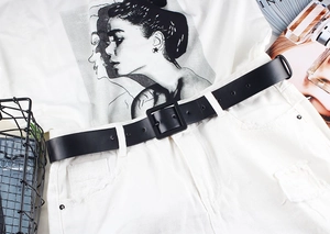 Close-up of minimalist black matte leather belt with square pin buckle on white denim