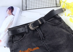 Detail of vintage silver carved buckle on black leather belt worn on denim jeans