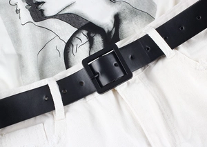 Detail of minimalist black leather belt with square pin buckle shown on white casual pants