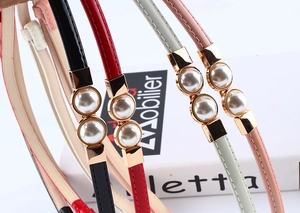 Detail of slim patent leather waist belts with gold ring buckles and pearl insets