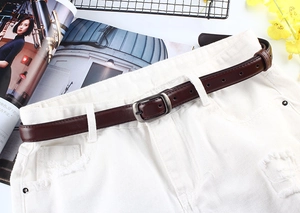 Détail de la ceinture fine en cuir marron foncé avec boucle carrée argentée sur un jean