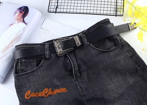 Detail of a vintage black leather belt with ornate silver floral buckle on denim fabric