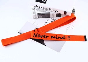 Detail of bright orange canvas belt featuring black Never mind text and metal buckle