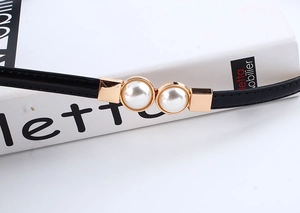 Detail of thin black patent leather belt with elegant gold pearl buckle on a white book