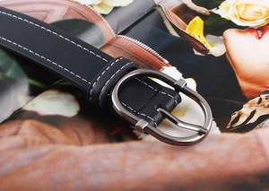 Détail de la ceinture en cuir noir avec double surpiqûre blanche et boucle ardillon ovale